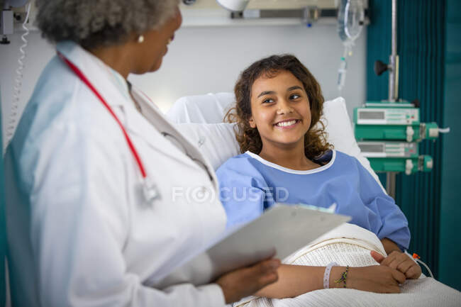 Chica sonriente paciente hablando con el médico en la habitación del hospital - foto de stock
