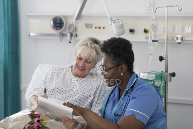 Female nurse discussing paperwork with senior patient in hospital room — Stock Photo