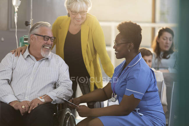 Жіноча медсестра розмовляє зі старшим пацієнтом чоловічої статі в інвалідному візку в клінічному вестибюлі — стокове фото