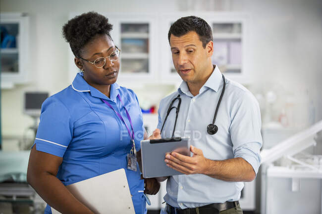 Médecin masculin avec tablette numérique parlant avec une infirmière à l'hôpital — Photo de stock