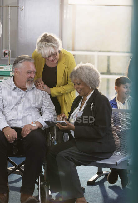 Médecin avec tablette numérique parlant au couple dans le hall de la clinique — Photo de stock