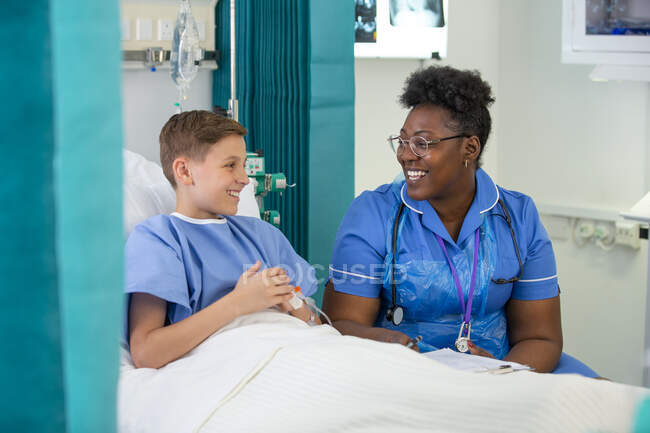 Жіноча медсестра розмовляє з пацієнтом-хлопчиком у лікарняній кімнаті — стокове фото