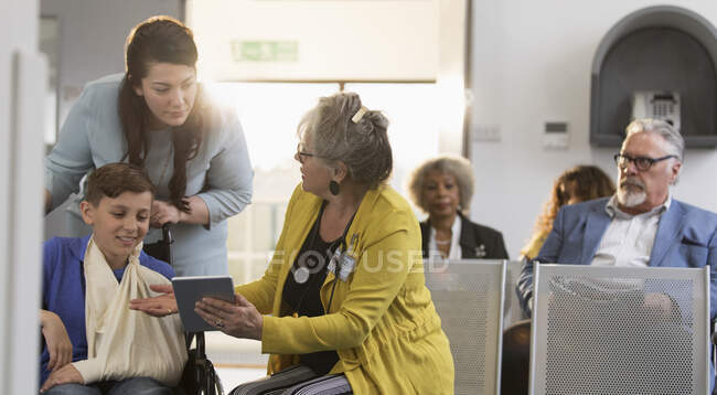 Doctora con tableta digital hablando con la madre y el niño en el vestíbulo de la clínica - foto de stock