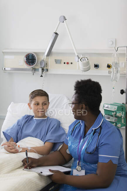 Female nurse with clipboard talking with boy patient in hospital room — Stock Photo