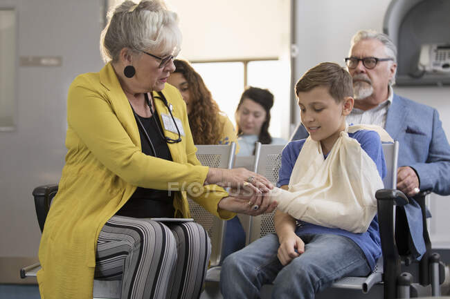 Médica examinando mão de menino paciente com braço na funda no lobby clínica — Fotografia de Stock