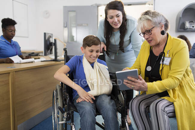 Жінка-лікар з цифровим планшетом розмовляє з матір'ю та пацієнтом-хлопчиком у інвалідному кріслі у вітальні клініки — стокове фото
