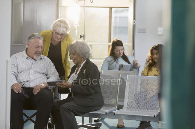 Médecin avec tablette numérique parlant au couple dans le hall de la clinique — Photo de stock