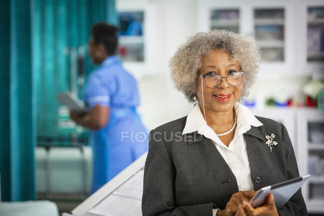 Portrait confident senior female doctor with digital tablet in hospital — Stock Photo