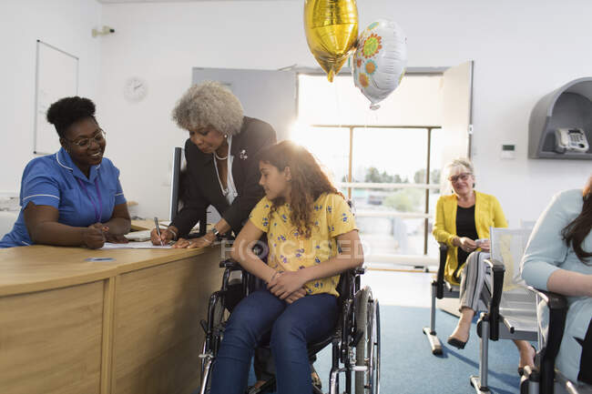 Chica paciente en silla de ruedas registrándose en la recepción de la clínica - foto de stock