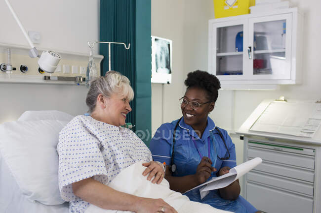 Female nurse talking with senior patient in hospital room — Stock Photo