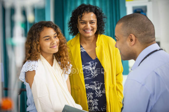 Pediatra masculino hablando con paciente chica con brazo en honda en sala de examen - foto de stock