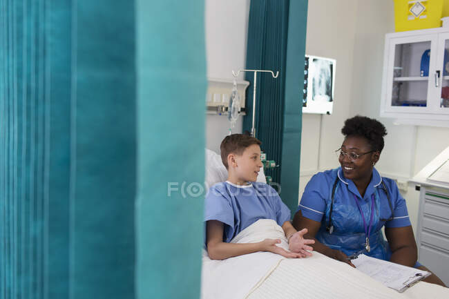 Жіноча медсестра розмовляє з пацієнтом хлопчика в лікарняній кімнаті — стокове фото