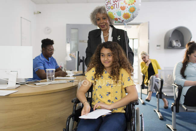 Woman pushing girl in wheelchair in clinic — Stock Photo