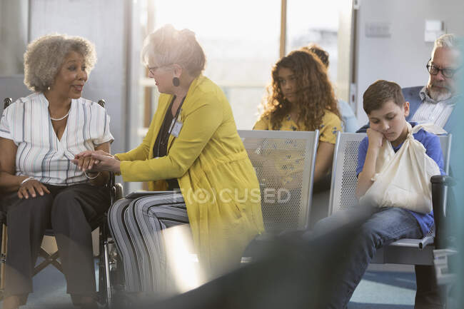Женщина-врач осматривает руку пожилого пациента в инвалидном кресле в холле клиники — стоковое фото