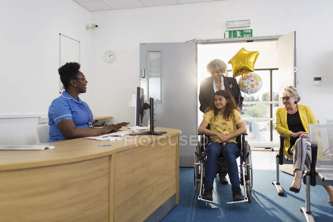 Mulher empurrando paciente menina em cadeira de rodas na recepção clínica — Fotografia de Stock