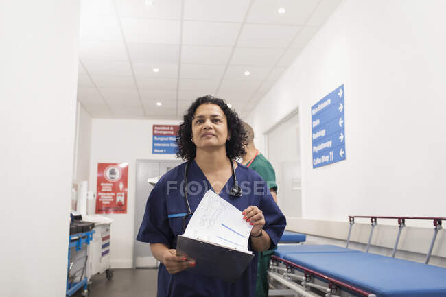 Confident female doctor with medical chart making rounds in hospital corridor — Stock Photo