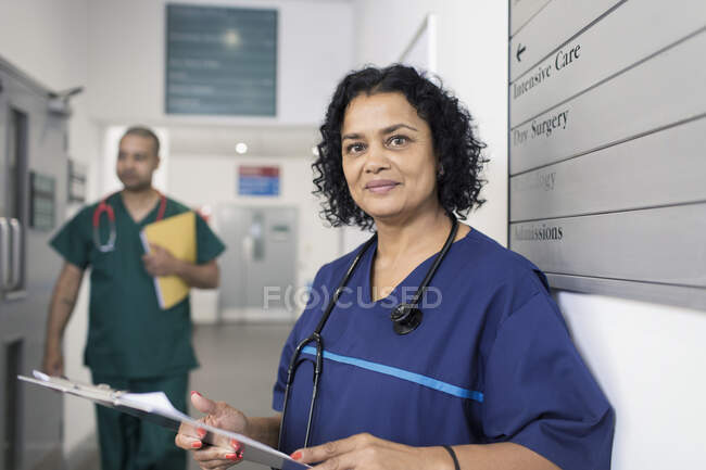 Retrato confiado médico femenino con historial médico, haciendo rondas en el pasillo del hospital - foto de stock