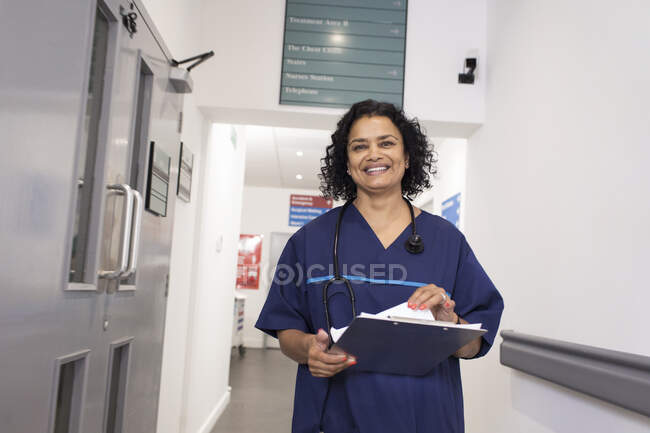 Портрет посміхається, впевнена жінка-лікар з медкартою, вирушає в похід по лікарняному коридору — стокове фото