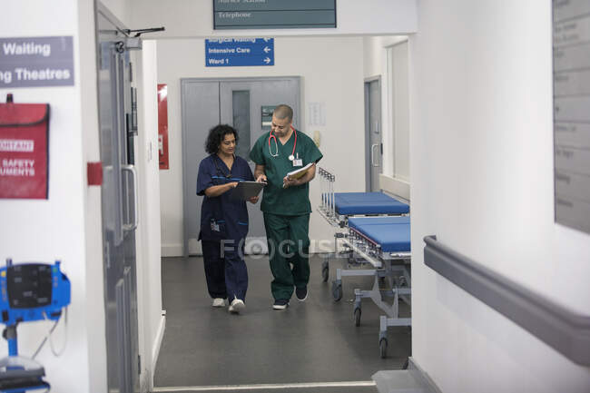 Médico y cirujano discutiendo historia clínica, caminando en el pasillo del hospital - foto de stock