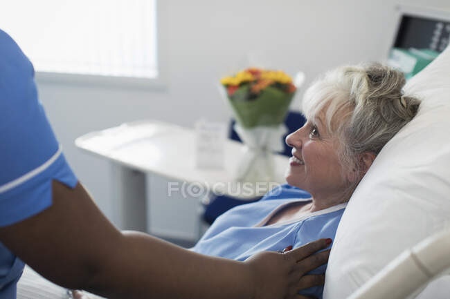 Pflegende Krankenschwester tröstet Seniorin, die im Krankenhausbett ruht — Stockfoto