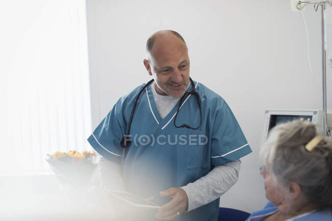 Doctor con tableta digital haciendo rondas, hablando con paciente mayor en la habitación del hospital - foto de stock