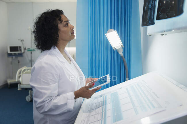 Сосредоточенная женщина-врач с цифровым планшетом, исследующая рентген в больничной палате — стоковое фото