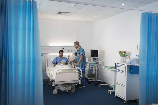 Enfermeira do sexo masculino conversando com o paciente usando tablet digital na cama do hospital — Fotografia de Stock