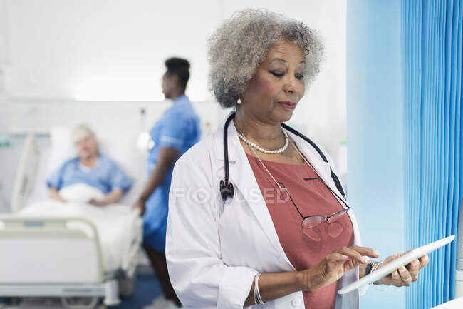 Médico senior femenino usando tableta digital en la habitación del hospital - foto de stock