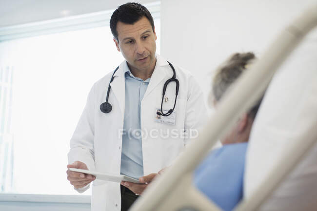 Médico con tableta digital haciendo rondas, hablando con paciente en cama de hospital - foto de stock