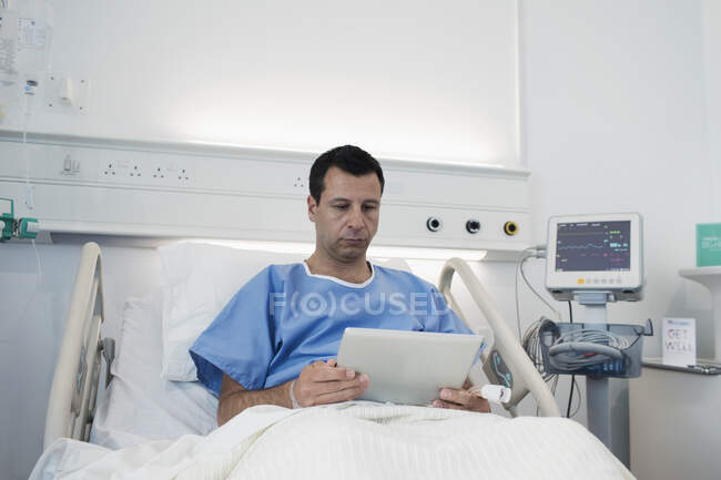 Male patient using digital tablet, resting in hospital bed — Stock Photo