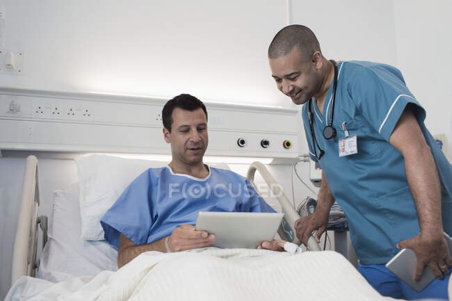 Пациент с цифровой планшетом разговаривает с медсестрой в больничной палате — стоковое фото