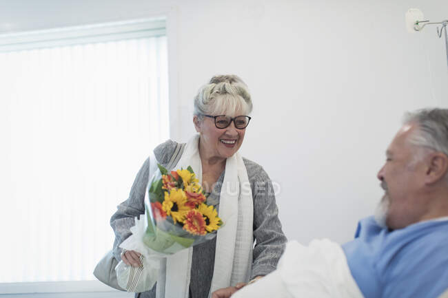 Счастливая пожилая женщина приносит букет цветов мужу выздоравливая в больничной палате — стоковое фото
