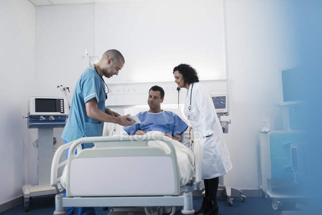 Médico e enfermeiro com tablet digital fazendo rondas, conversando com o paciente no quarto do hospital — Fotografia de Stock