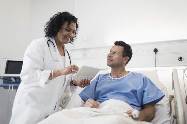 Médico con tableta digital haciendo rondas, hablando con el paciente en la habitación del hospital - foto de stock