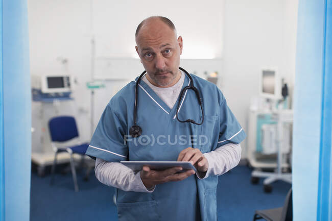 Portrait confident, serious male doctor using digital tablet in hospital room — Stock Photo