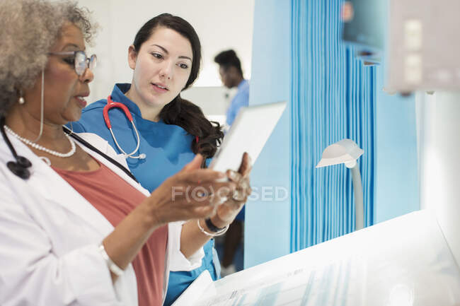 Doctora y enfermera usando tableta digital, hablando en la habitación del hospital - foto de stock