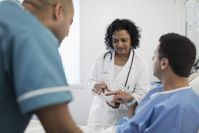 Doctor with digital tablet making rounds, talking with patient in hospital bed — Stock Photo