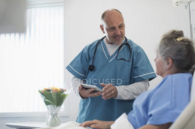 Arzt mit digitalem Tablet macht Runde, spricht mit Seniorin im Krankenzimmer — Stockfoto