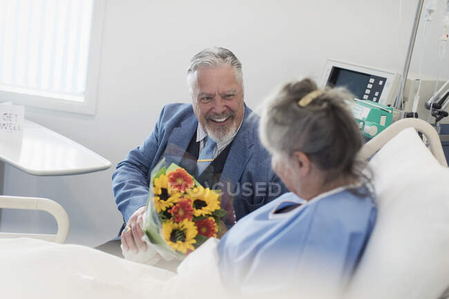 Happy senior man with flower bouquet visiting wife in hospital — Stock Photo