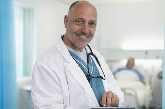 Portrait confident, smiling male doctor using digital tablet in hospital room — Stock Photo