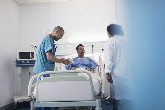 Médicos com tablet digital fazendo rondas, conversando com o paciente no quarto do hospital — Fotografia de Stock