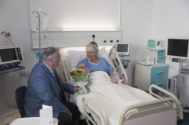 Senior mit Blumenstrauß besucht Ehefrau, die im Krankenhauszimmer ruht — Stockfoto