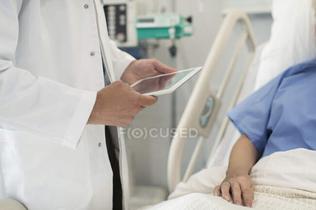Médico con tableta digital haciendo rondas, revisando al paciente en la cama del hospital - foto de stock