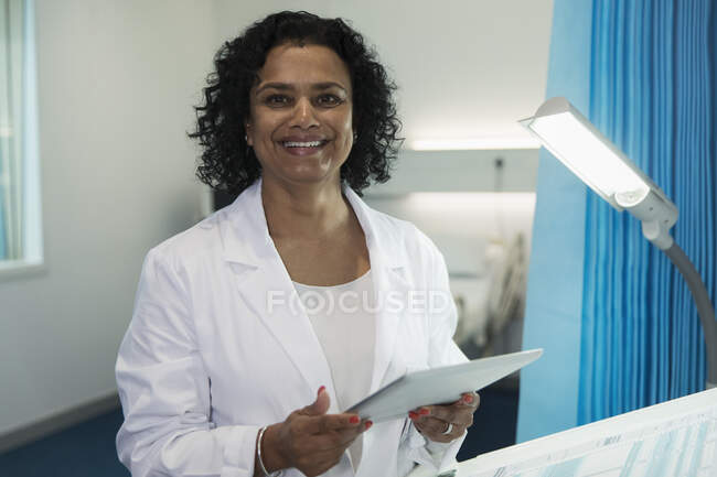 Портрет впевнена, усміхнена жінка-лікар використовує цифровий планшет в лікарняній кімнаті — стокове фото