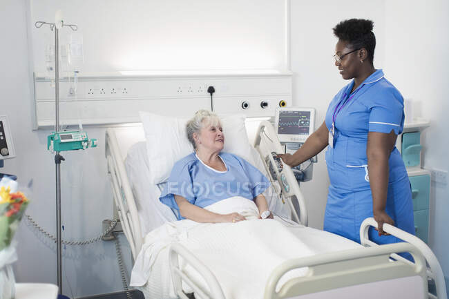 Enfermera hablando con paciente mayor en la habitación del hospital - foto de stock