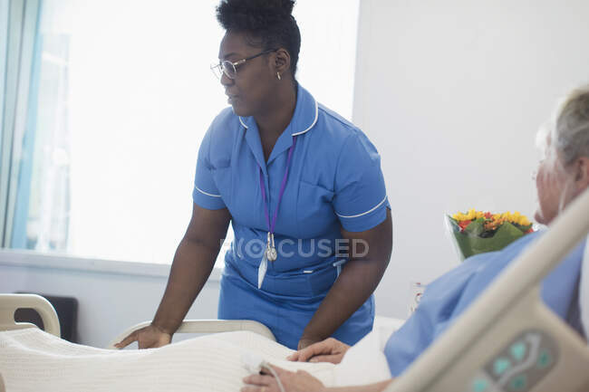 Female nurse helping patient in hospital bed — Stock Photo