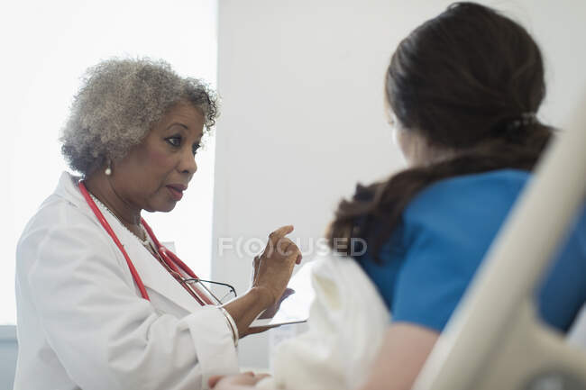 Médica sênior com tablet digital fazendo rondas, conversando com paciente na cama do hospital — Fotografia de Stock