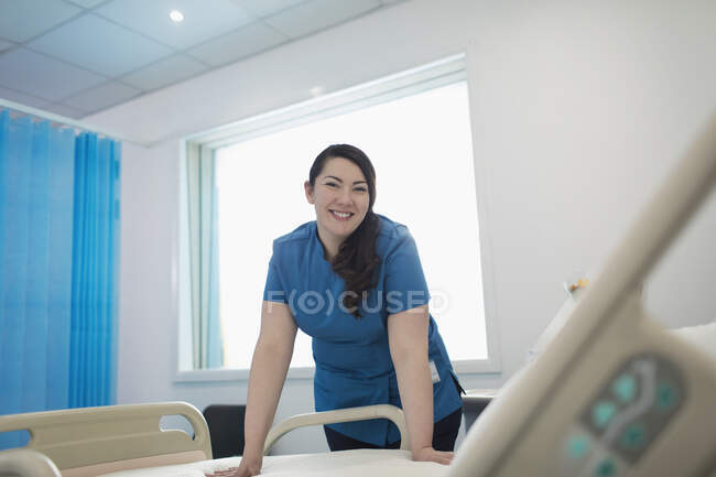 Уверенная в себе, улыбающаяся медсестра, заправляющая больничную кровать — стоковое фото