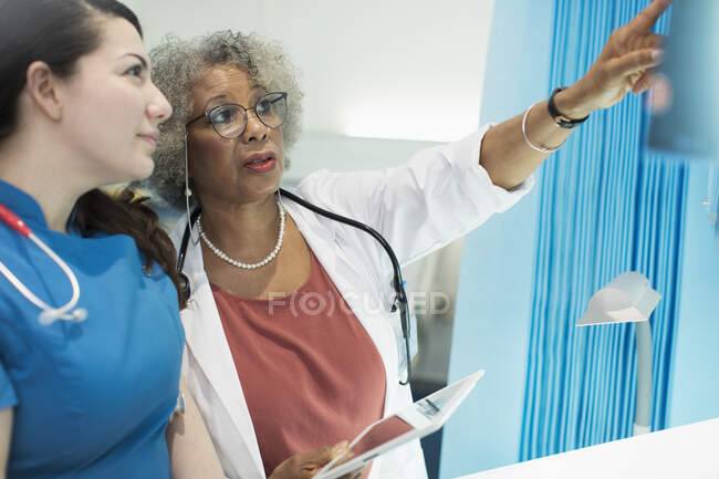 Doctora y enfermera con tableta digital hablando en la habitación del hospital - foto de stock