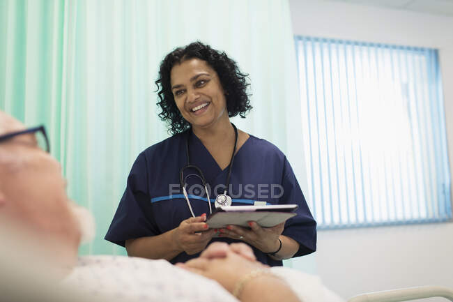 Медсестра с цифровым планшетом делает обходы, разговаривает с пациентом в больничной палате — стоковое фото